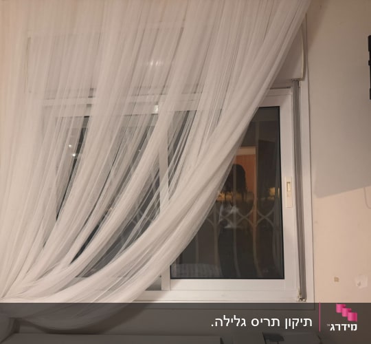 חלון הזזה מאלומיניום לבן מוסתר בחלקו על ידי וילון